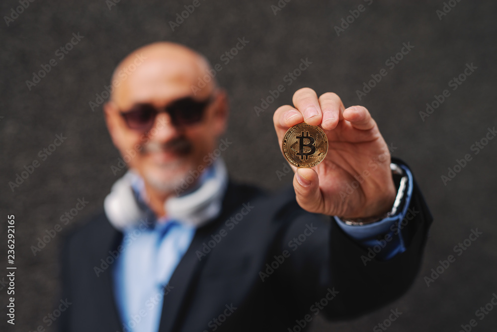 Fototapeta premium Bearded senior adult wealthy businessman holding bit-coin. Selective focus on bit-coin.