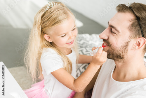 adorable little daughter applying makeup to happy father at home