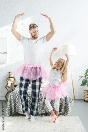 happy father and adorable little daughter in pink tutu skirts dancing and smiling each other