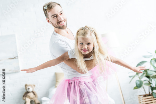 happy father and daughter in pink tutu skirts dancing at home