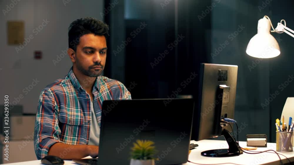 business, technology and creative people concept - young indian man with laptop computer working at dark night office