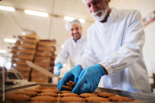 Close up of man picking cookies while other one packing in boxed. Food factory interior.