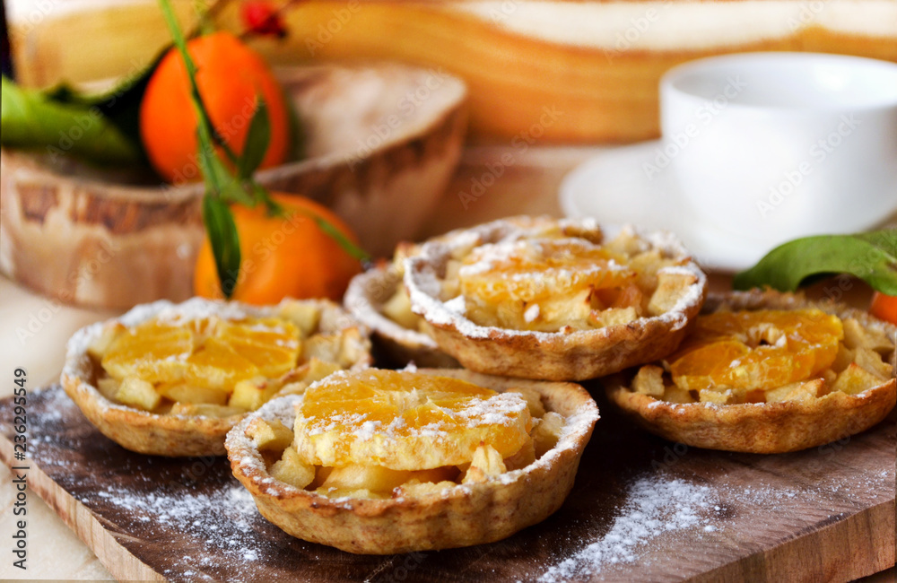 Apple and Orange Tarts , decorated powdered sugar, on wooden board. A simple tart topped with buttery soft apples, orange slice and sugar powder