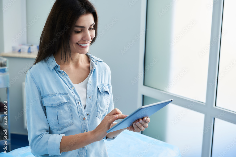 Waist up photo of happy woman filling out questionnaire while using tablet in beauty clinic. Copy space on right side Waist up photo of happy woman filling out questionnaire while using tablet in beauty clinic. Copy space on right side
