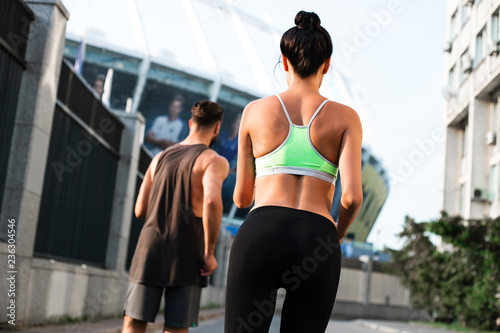 Another mile. Rear view of young beautiful couple in sportswear jogging against industrial city view