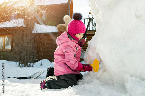 Children playing together in yard after snowfall in winter. Group of kids bilding figures and snowman with shovels and other tools outdoors. Child winter activities