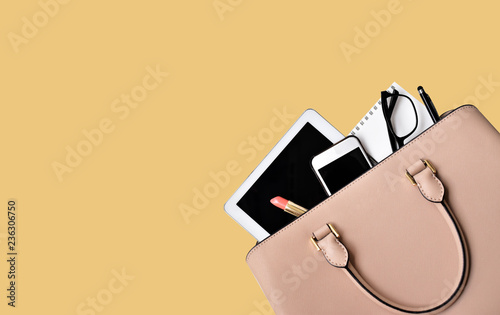 Business woman's everyday-life travel accessories flat lay on yellow background with formal beige handbag, a cellphone, blank notepad, luxury pen, glasses and lipstick, copy space for text