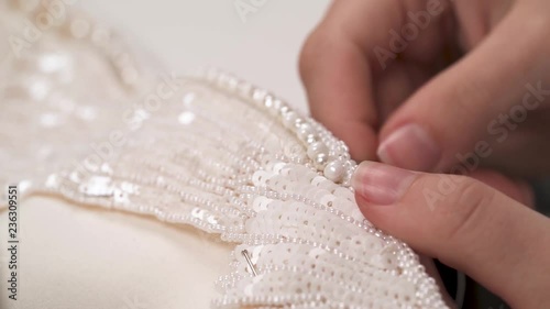 A dolly of woman's hands sewing beaded lace down the wedding dress