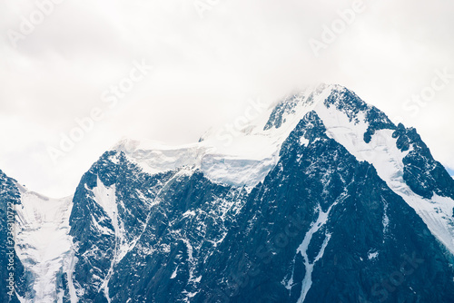 Snowy mountain top in overcast sky. Rocky ridge in mist. Atmospheric minimalistic landscape of majestic nature.
