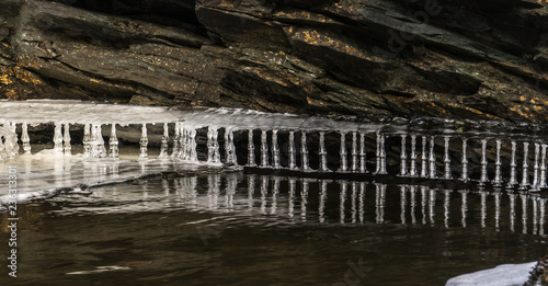ice icicles of freakish form between stones and the river
