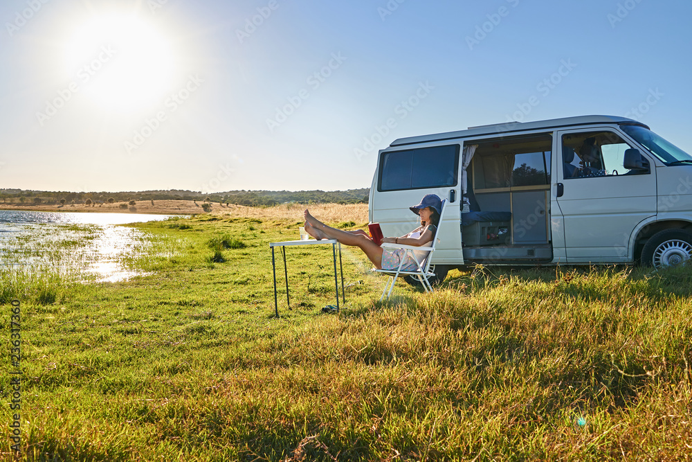 Lady sitting on chair near table and reading book on shore of river Lady sitting on chair near table and reading book on shore of river