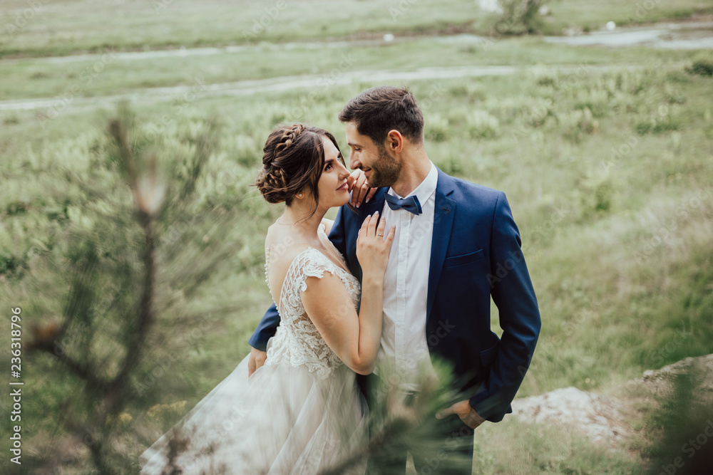 Young wedding couple enjoying romantic moments outside on a summer meadow.Bride and groom at wedding day walking outdoors in beautiful space.Happy newlywed woman and man embracing in green park.
