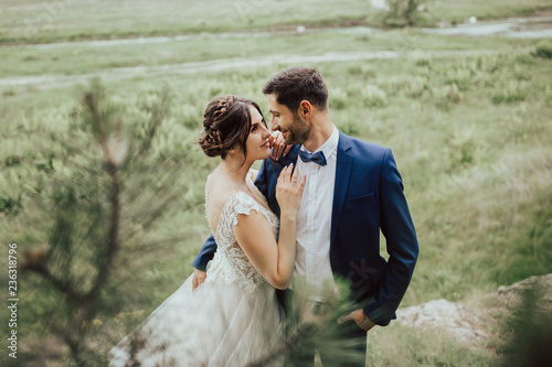 Obraz na płótnie Young wedding couple enjoying romantic moments outside on a summer meadow.Bride and groom at wedding day walking outdoors in beautiful space.Happy newlywed woman and man embracing in green park. w salonie