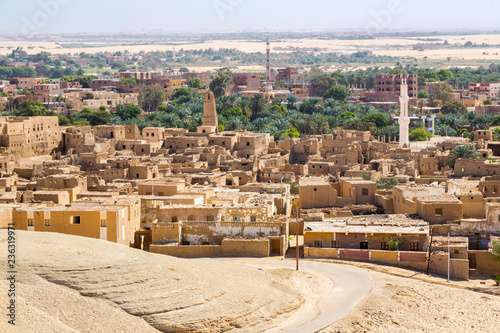 Oasis with ruins of ancient middle eastern Arab town built of mud bricks, old mosque with minaret. New city in background. Al Qasr, Dakhla Oasis, Western Desert, New Valley Governorate, Egypt, Africa.