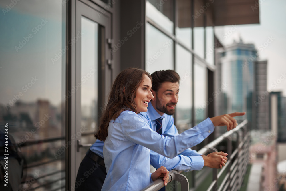 Obraz premium Concept of friendly communication between coworkers. Waist up portrait of smiling woman showing something to man from office balcony while have work break