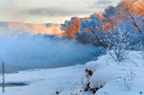 Winter landscape of trees and river in a foggy morning. Frost and cold and sunshine.