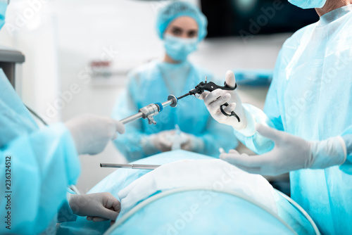 Close up of male and female hands holding laparoscopic grasper with trocar. Female medical worker holding oxygen mask on patient face on blurred background photo