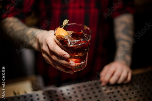 Barman holding a glass of whiskey cocktail decorated with orange peel