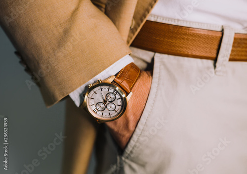 Closeup fashion image of luxury brown watch on wrist of man.body detail of a business man.Man's hand in pants pocket closeup at white background.Man wearing beige jacket and white shirt.Not isolated