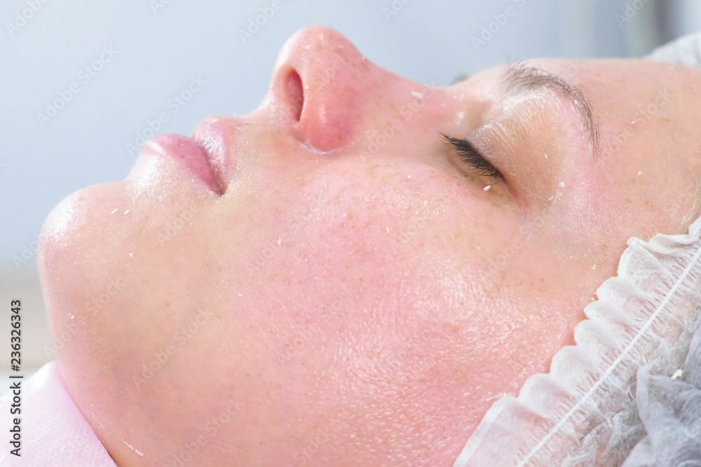 Naklejka premium Rolls the mask on the woman's face. Cosmetologist facial treatment. Close-up.