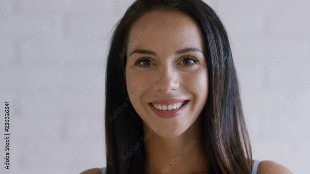 Attractive young female with brown hair smiling and looking at camera while standing on white background