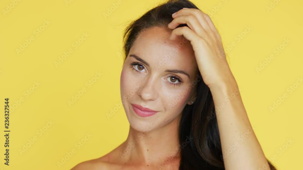 Lovely young woman with brown hair cheerfully smiling and looking at camera while standing on bright yellow background Lovely young woman with brown hair cheerfully smiling and looking at camera while standing on bright yellow background