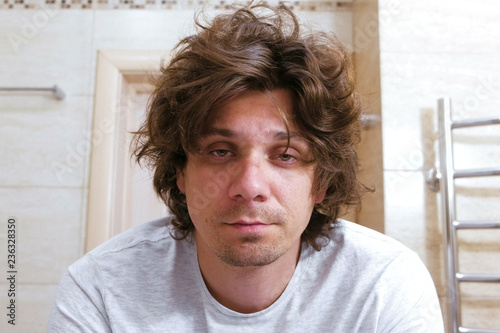 Canvas Print Sleepy shaggy young man looks at the mirror in bathroom in the morning