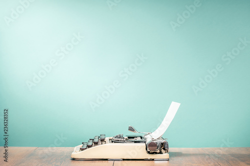 Fototapeta Retro classic typewriter from circa 1950s with sheet of paper on wooden desk front aquamarine wall background