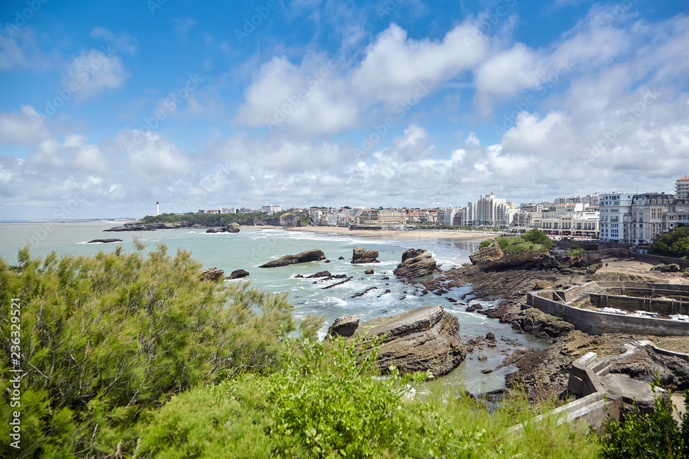 Fototapeta premium Cityscape of Biarritz, France: Old stone harbor, buildings and sandy beaches. Summer sunny day with blue sky and white clouds