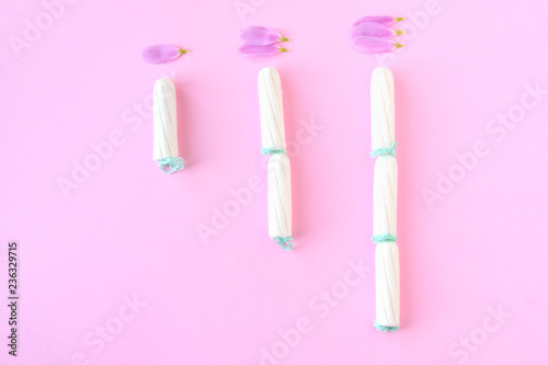 Tampons with selective focus on blurred pink background with pink flower petals. Woman hygiene for period days, menstrual mothly cycle. Protective care for woman health.