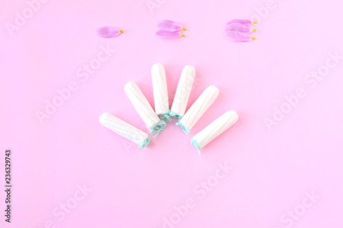 Tampons with selective focus on blurred pink background with pink flower petals. Woman hygiene for period days, menstrual mothly cycle. Protective care for woman health.