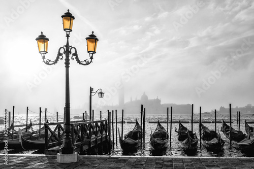 Black and white photo of gondolas in Venice at sunrise with Saint Giorgio island in morning fog, as seen from San Marco square