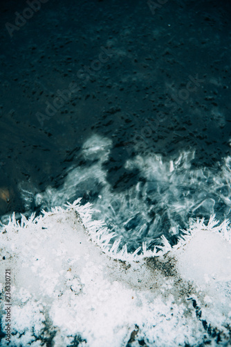 Ice fragments under thin layer of frozen river water. Dark blue natural background
