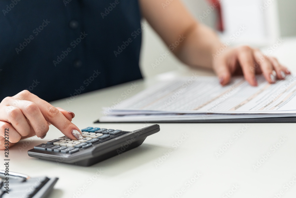 Women's hands count on the calculator and fill out the form. Women's hands count on the calculator and fill out the form.
