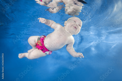 Funny face portrait of little baby girl swimming and diving underwater with fun in pool on a blue water background. Healthy family lifestyle and children water sports activity.