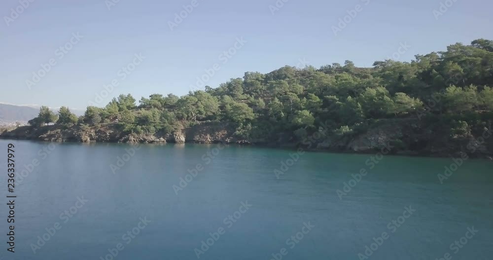 Forward aerial drone video rising over ocean water, waterfront forest to reveal high angle view of natural bay, harbor and cityscape of Fethiye, Turkey. 4k at 23.97fps Forward aerial drone video rising over ocean water, waterfront forest to reveal high angle view of natural bay, harbor and cityscape of Fethiye, Turkey. 4k at 23.97fps