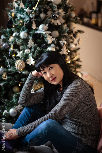 Portrait of adult asian woman in casual warm clothes near christmas tree decoration