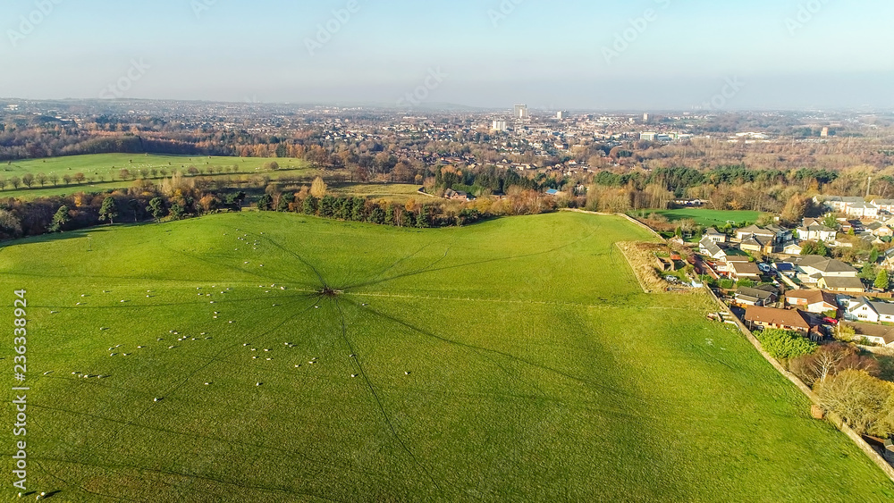 Aerial image over a green field with grazing sheep to the townscape of Coatbridge.