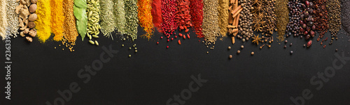 Variety condiments and herbs scattered on background of  black table. Heaps Indian spices on chalkboard with empty space.