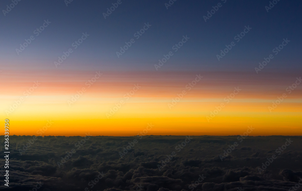 Colorful sunset over clouds. Orange and blue sky cloudscape views from airplane. Background texture, horizon concepts