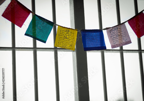 Colorful Tibetan prayer flags behind black and white bars background. Freedom symbol, hope in prison concept