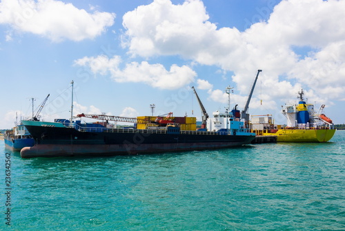 Loading and unloading of containers on commercial cargo ship in sea port on a bright sunny day. Background for import ,export cargo, nautical vessel transport and industry logistic. Safety first.