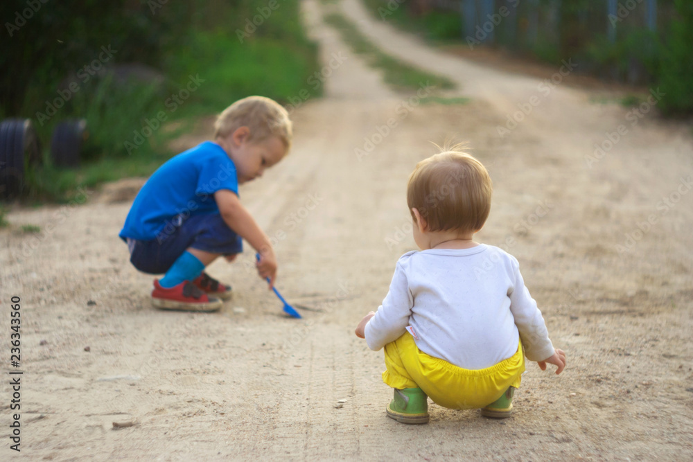 Small children play on the unpaved roadway of a rural settlement. Child safety on the road. Dangerous games on the street. The guys use the sandy road like a sandbox. Small children play on the unpaved roadway of a rural settlement. Child safety on the road. Dangerous games on the street. The guys use the sandy road like a sandbox.