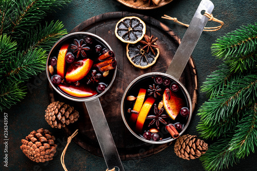 Foto hot mulled wine cooked in two saucepan with spices, orange and cranberries on th