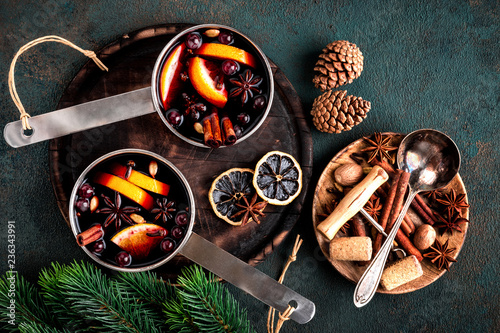 hot mulled wine cooked in two saucepan with spices, orange and cranberries on the table with Christmas fir twigs on a dark background