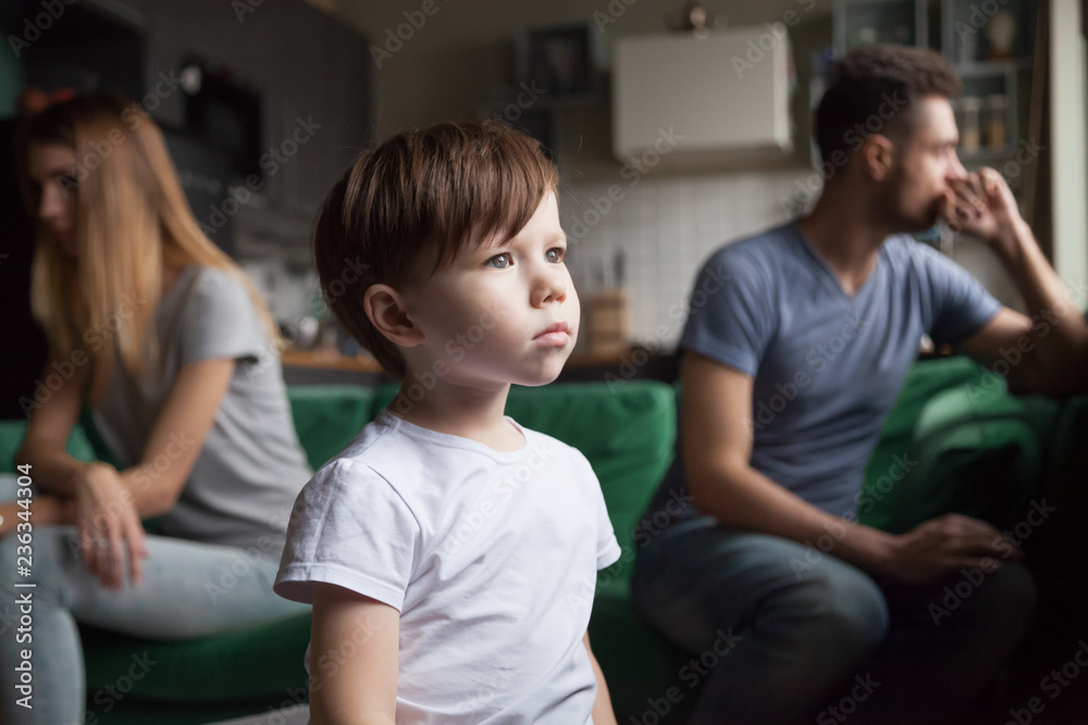 Upset frustrated little boy tired of parents fight, toddler son looking out window reaming that family conflicts would stop while parents sitting separately on sofa, suffering from mom and dad quarrel Upset frustrated little boy tired of parents fight, toddler son looking out window reaming that family conflicts would stop while parents sitting separately on sofa, suffering from mom and dad quarrel