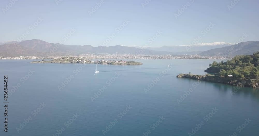 Forward descending aerial drone video low over ocean water in natural harbor and distant oceanfront cityscape, mountain range of Fethiye, Turkey. 4k at 23.97fps Forward descending aerial drone video low over ocean water in natural harbor and distant oceanfront cityscape, mountain range of Fethiye, Turkey. 4k at 23.97fps