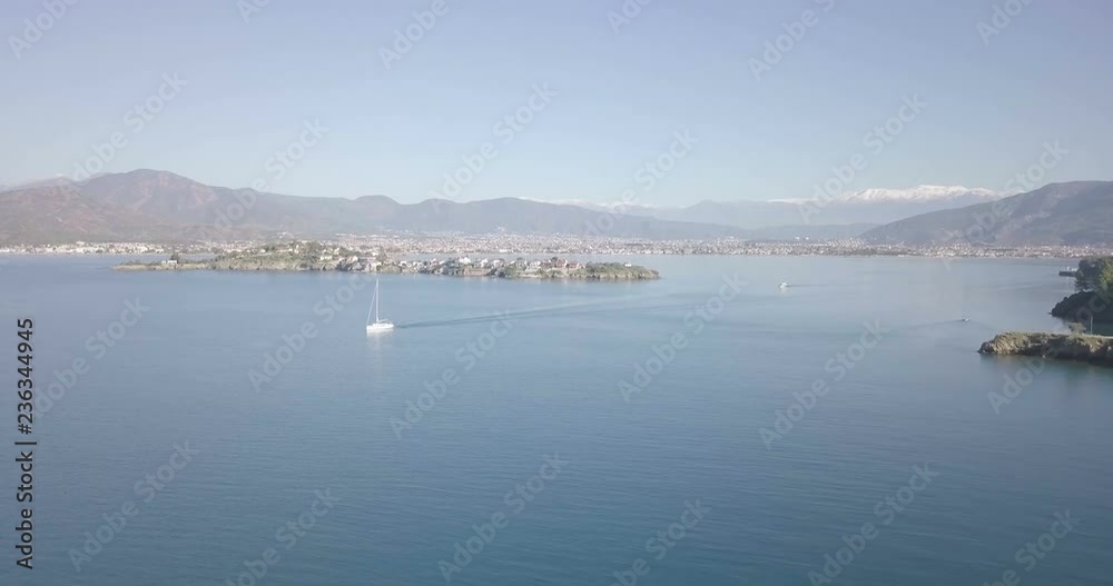 Forward aerial drone video above ocean water passing sailboat towards Fethiye Adasi island in natural harbor with scenic mountain landscape view behind Fethiye, Turkey. 4k at 23.97fps Forward aerial drone video above ocean water passing sailboat towards Fethiye Adasi island in natural harbor with scenic mountain landscape view behind Fethiye, Turkey. 4k at 23.97fps