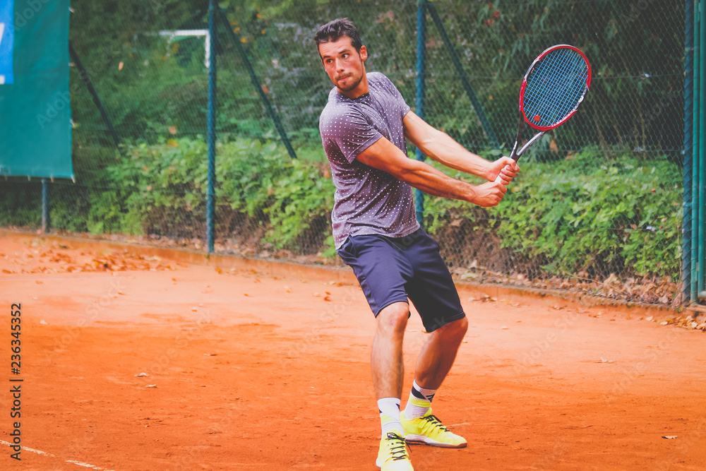 Junger Tennisspieler holt zu einem Rückhandschlag aus - gespielt auf einem  Sandplatz Court Stock Photo | Adobe Stock