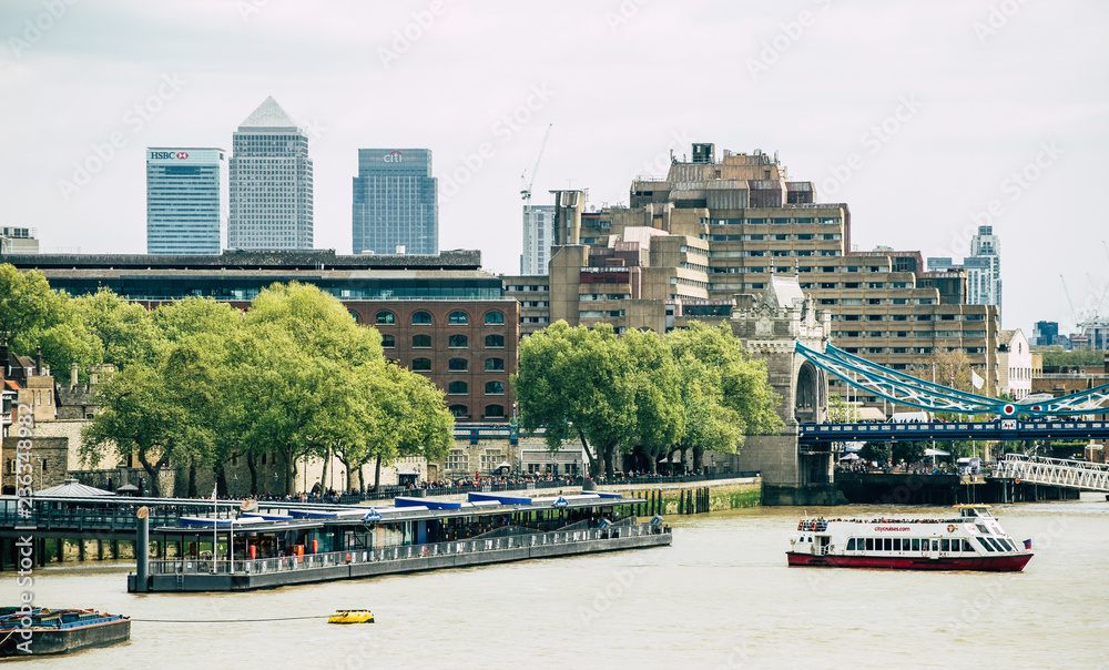 A boat next to the Tower Bridge pier with Canary Wharf in the background